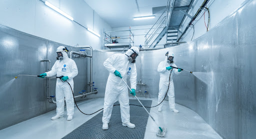 A clean, industrial yet highly hygienic view of certified property maintenance workers in full sterile protective suits and headgear thoroughly sanitizing a sparkling clean stainless steel underground municipal water cistern, bright industrial white-blue lighting showcasing pristine hygiene standards.
